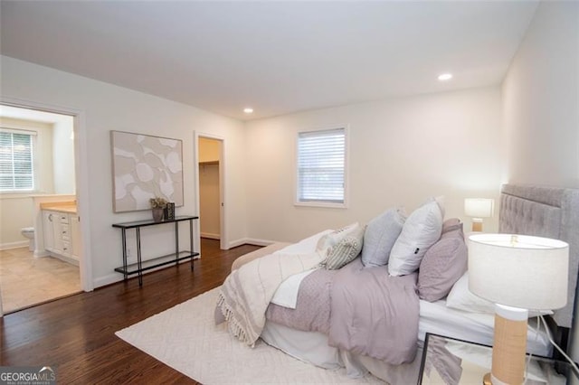 bedroom featuring baseboards, ensuite bath, wood finished floors, a spacious closet, and recessed lighting