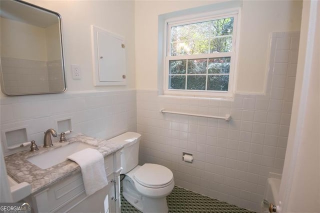 full bathroom with tile patterned flooring, toilet, vanity, tile walls, and wainscoting