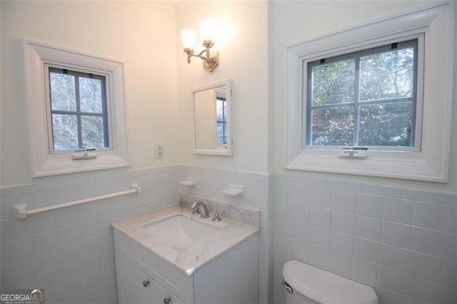 half bathroom featuring a wealth of natural light, wainscoting, vanity, and toilet