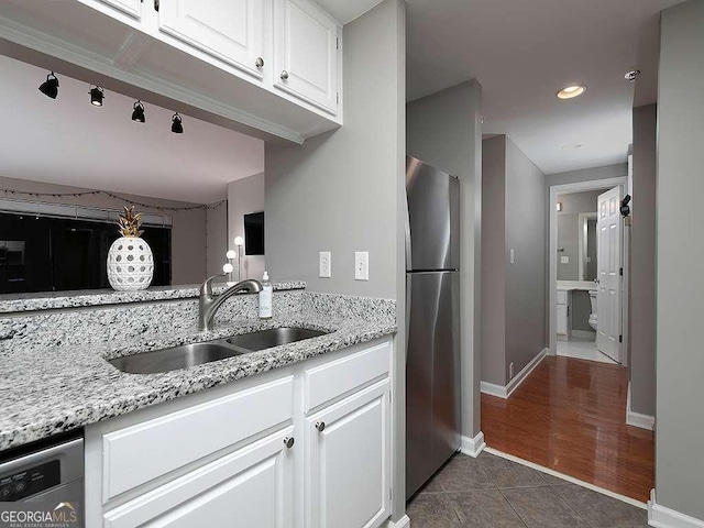 kitchen featuring dark tile patterned flooring, light stone counters, stainless steel appliances, white cabinetry, and a sink