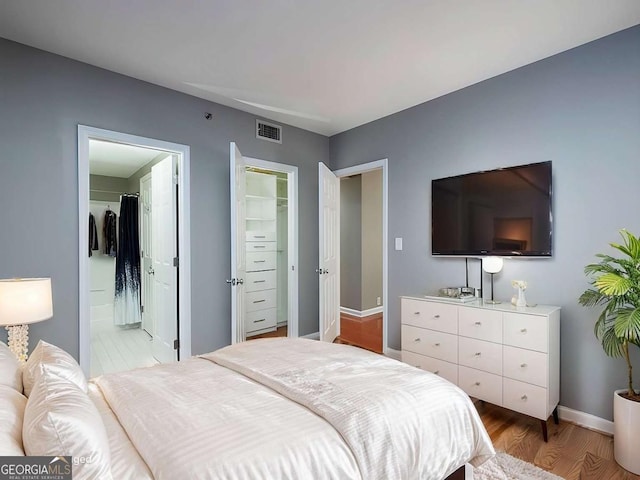 bedroom with visible vents, baseboards, a closet, light wood-type flooring, and a walk in closet