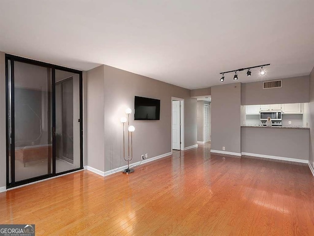 unfurnished living room with light wood-type flooring, rail lighting, visible vents, and baseboards