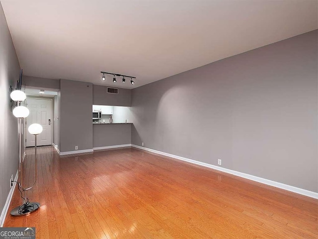 unfurnished living room with track lighting, baseboards, visible vents, and light wood finished floors