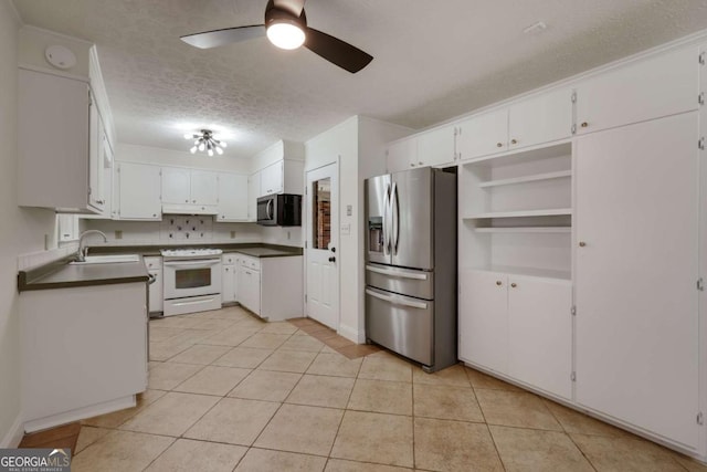 kitchen with light tile patterned floors, dark countertops, appliances with stainless steel finishes, a textured ceiling, and a sink