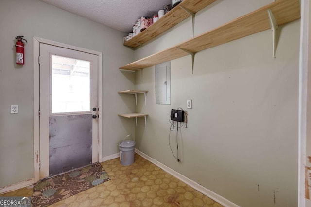 washroom featuring baseboards, electric panel, a textured ceiling, and light floors