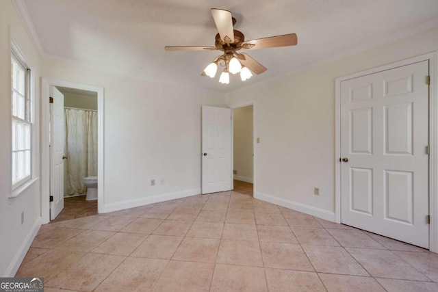 unfurnished bedroom featuring light tile patterned floors, ornamental molding, ceiling fan, ensuite bath, and baseboards