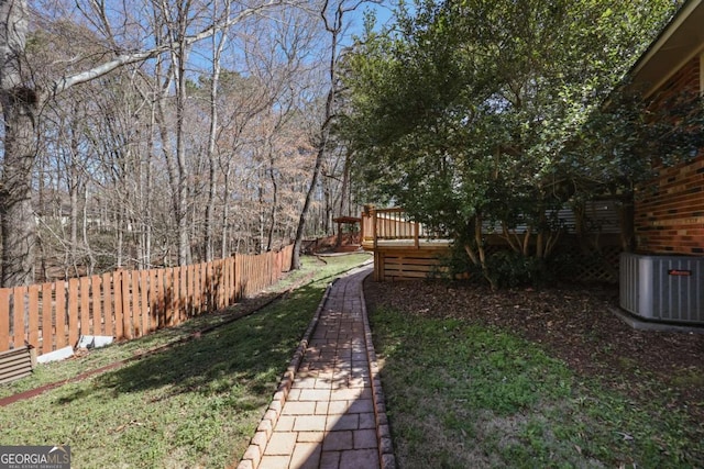 view of yard with fence, a deck, and central AC unit