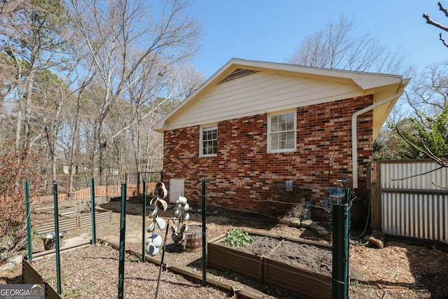 view of side of property with brick siding, fence, and a garden