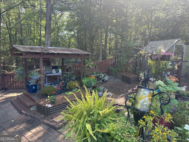 wooden deck featuring a greenhouse, an outdoor structure, fence, a garden, and a forest view