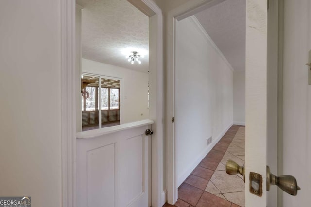 corridor featuring baseboards, ornamental molding, a textured ceiling, and tile patterned floors