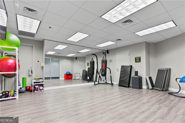 exercise room with a drop ceiling, visible vents, baseboards, and wood finished floors