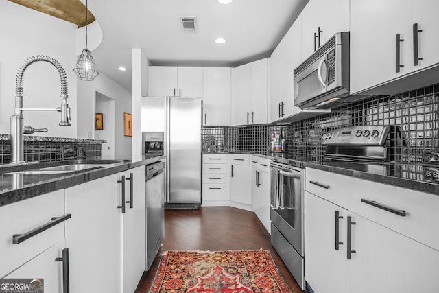 kitchen with visible vents, a sink, stainless steel appliances, white cabinets, and decorative backsplash