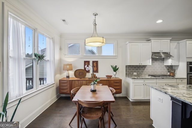 kitchen with under cabinet range hood, dark wood-type flooring, visible vents, tasteful backsplash, and crown molding