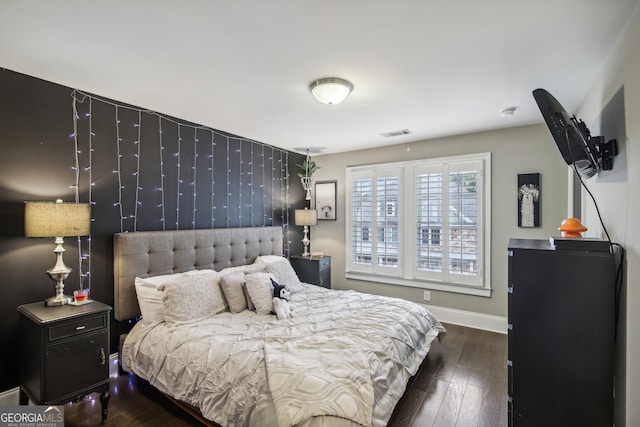 bedroom featuring an accent wall, visible vents, baseboards, and wood finished floors