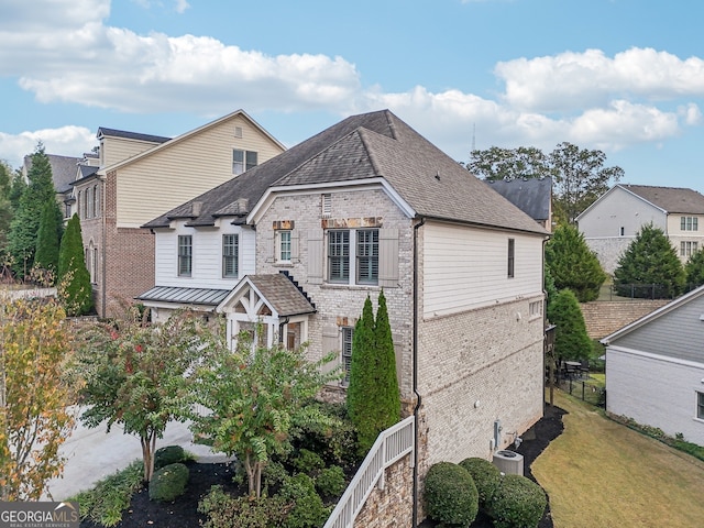 view of front of property featuring metal roof, brick siding, a shingled roof, a front lawn, and a standing seam roof