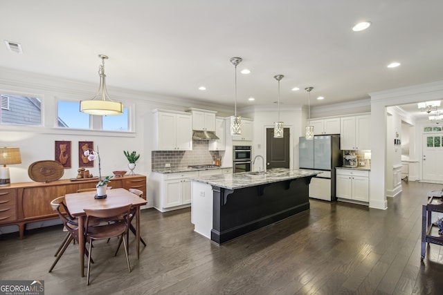 kitchen with under cabinet range hood, stainless steel appliances, a sink, ornamental molding, and decorative backsplash