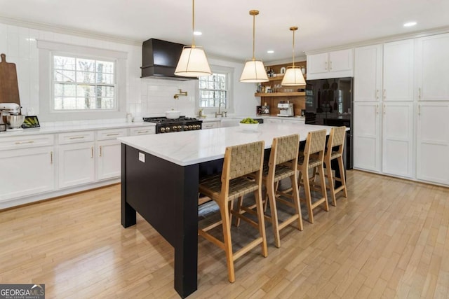 kitchen with stove, custom exhaust hood, white cabinetry, and light wood-style floors