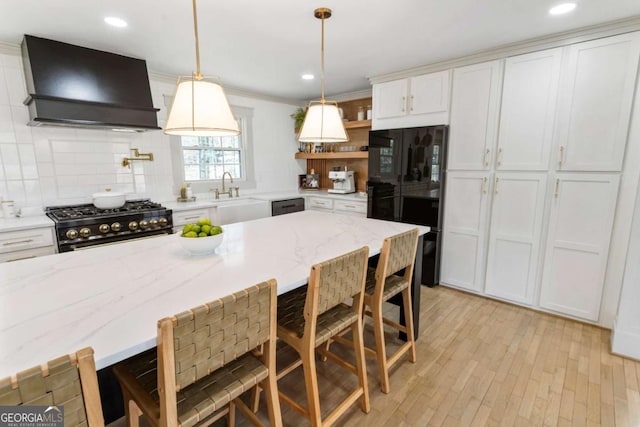 kitchen with a breakfast bar area, open shelves, white cabinetry, custom exhaust hood, and black appliances