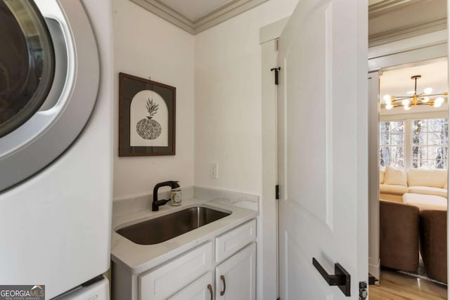 clothes washing area featuring cabinet space, stacked washer / dryer, ornamental molding, a chandelier, and a sink