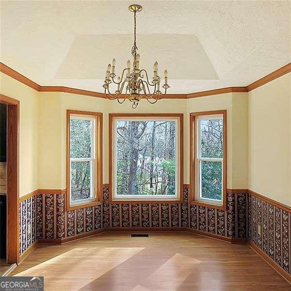 unfurnished dining area with wood finished floors, wainscoting, visible vents, and an inviting chandelier