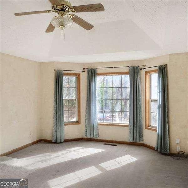 carpeted empty room with a textured ceiling, a raised ceiling, visible vents, and lofted ceiling