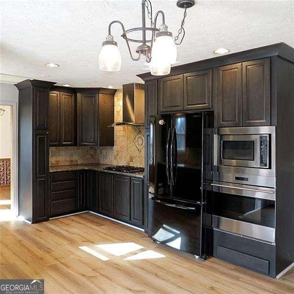 kitchen featuring dark brown cabinetry, wall chimney exhaust hood, hanging light fixtures, stainless steel appliances, and light wood-type flooring