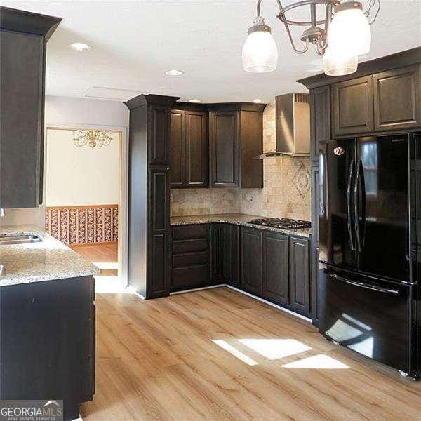 kitchen featuring dark brown cabinetry, light wood-type flooring, freestanding refrigerator, light stone countertops, and wall chimney exhaust hood