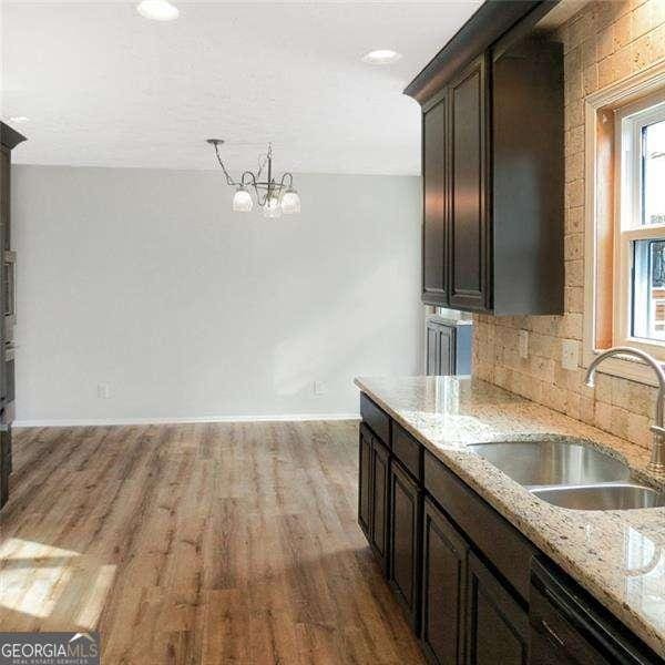 kitchen featuring a sink, black dishwasher, light wood-type flooring, backsplash, and light stone countertops