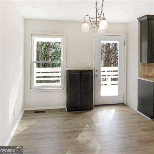 doorway to outside with light wood finished floors, visible vents, a textured ceiling, a chandelier, and baseboards