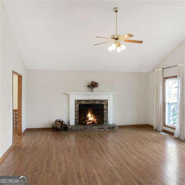 unfurnished living room featuring lofted ceiling, a fireplace, wood finished floors, and a ceiling fan