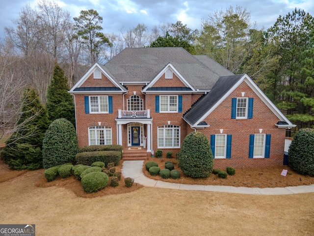 colonial house with brick siding, roof with shingles, and a balcony