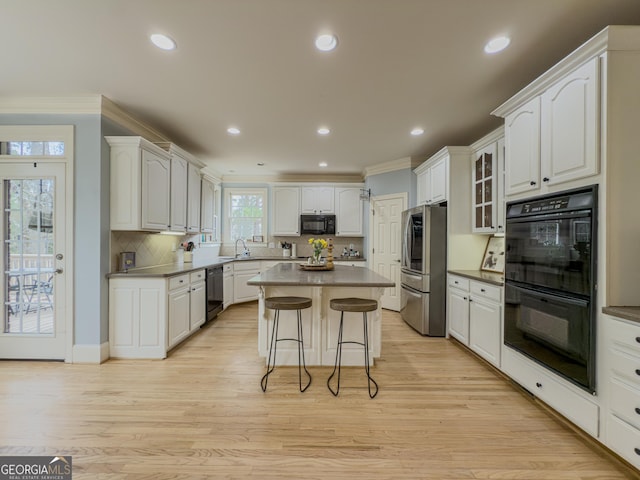 kitchen with black appliances, a sink, a breakfast bar area, crown molding, and light wood finished floors
