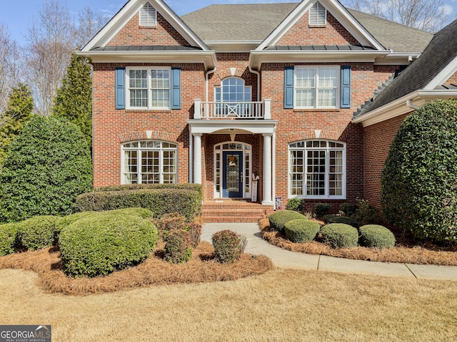 colonial inspired home featuring a balcony and brick siding