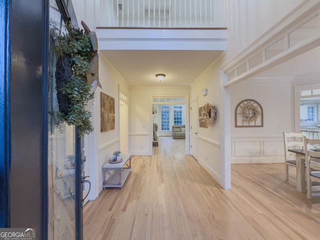 entryway with light wood-style flooring, a decorative wall, french doors, and ornamental molding