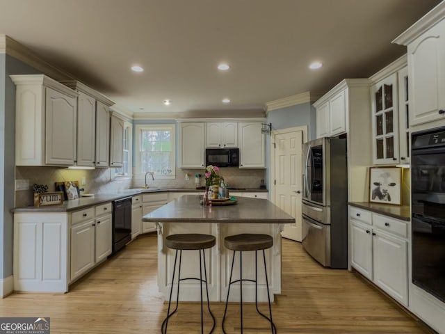 kitchen with black appliances, dark countertops, a breakfast bar area, crown molding, and glass insert cabinets