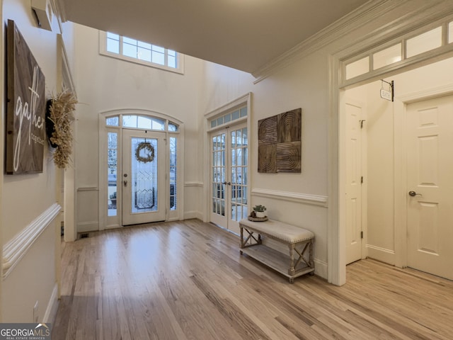 foyer featuring french doors, baseboards, light wood finished floors, and ornamental molding