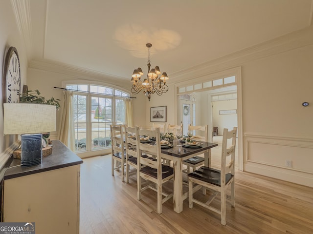 dining space featuring a chandelier, light wood-style flooring, wainscoting, and ornamental molding