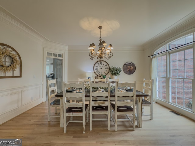 dining space featuring visible vents, light wood-style flooring, wainscoting, crown molding, and a chandelier