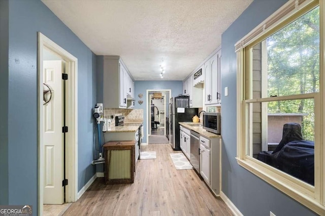 kitchen featuring a textured ceiling, stainless steel appliances, baseboards, light wood-type flooring, and tasteful backsplash