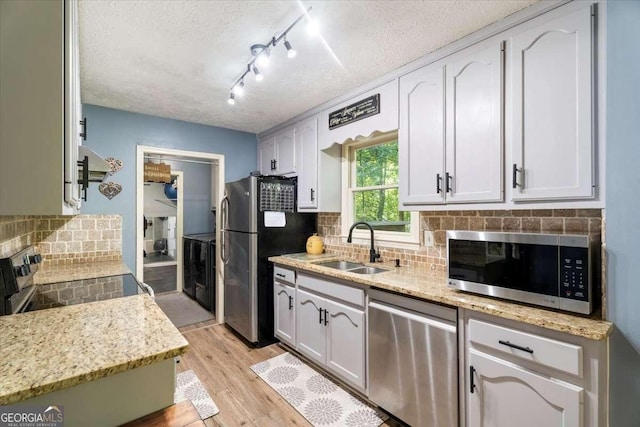 kitchen featuring a textured ceiling, light wood-style flooring, stainless steel appliances, a sink, and tasteful backsplash