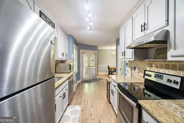 kitchen with stainless steel appliances, white cabinets, under cabinet range hood, and decorative backsplash