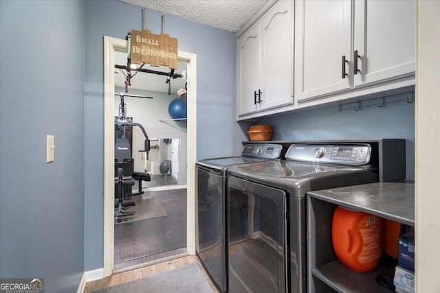 laundry room with cabinet space, wood finished floors, a textured ceiling, and washing machine and clothes dryer