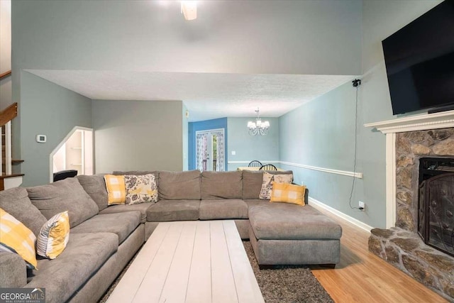 living room featuring stairway, wood finished floors, a textured ceiling, a fireplace, and a chandelier