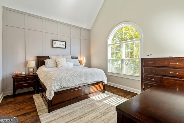 bedroom featuring a decorative wall, dark wood-style floors, baseboards, and high vaulted ceiling