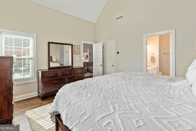 bedroom with visible vents, dark wood-type flooring, high vaulted ceiling, ensuite bath, and baseboards