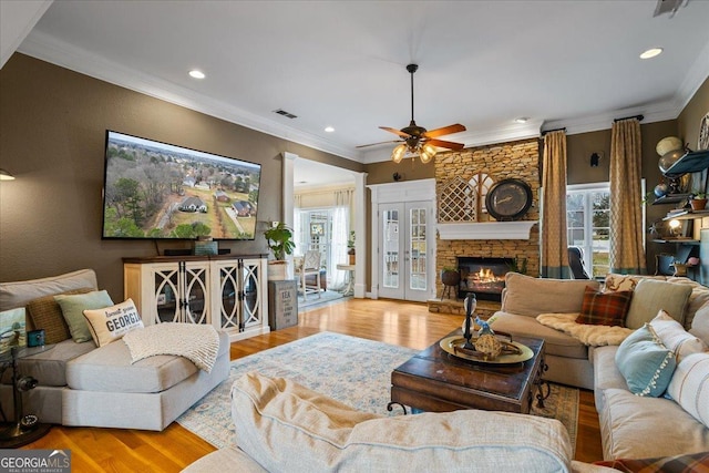 living room with ornamental molding, visible vents, a fireplace, and wood finished floors