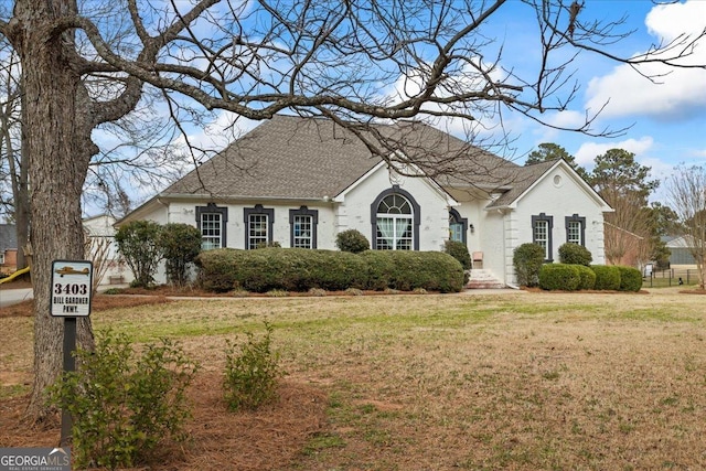 view of front of property featuring a front yard, brick siding, and roof with shingles