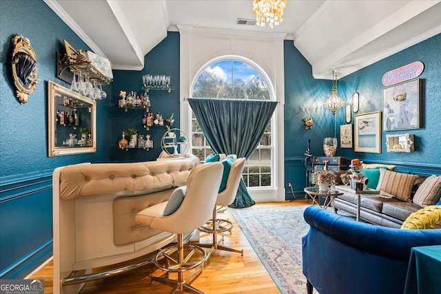 living area featuring lofted ceiling, visible vents, ornamental molding, wood finished floors, and a chandelier