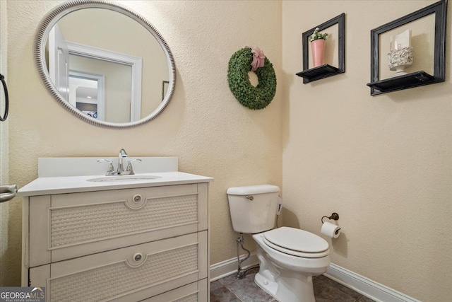 bathroom with baseboards, a textured wall, vanity, and toilet