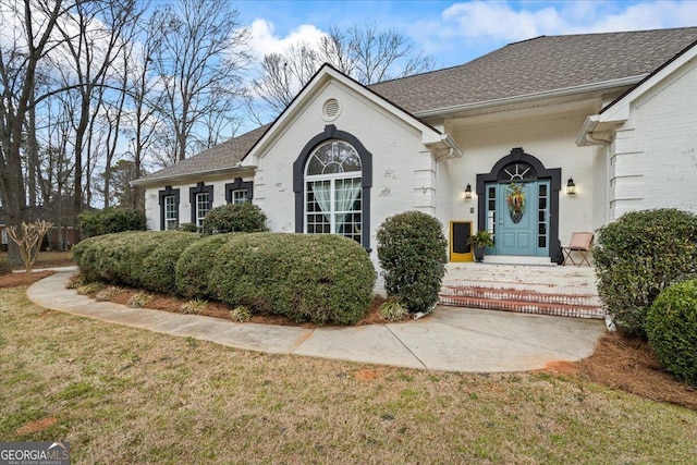 exterior space featuring brick siding, a front lawn, and roof with shingles